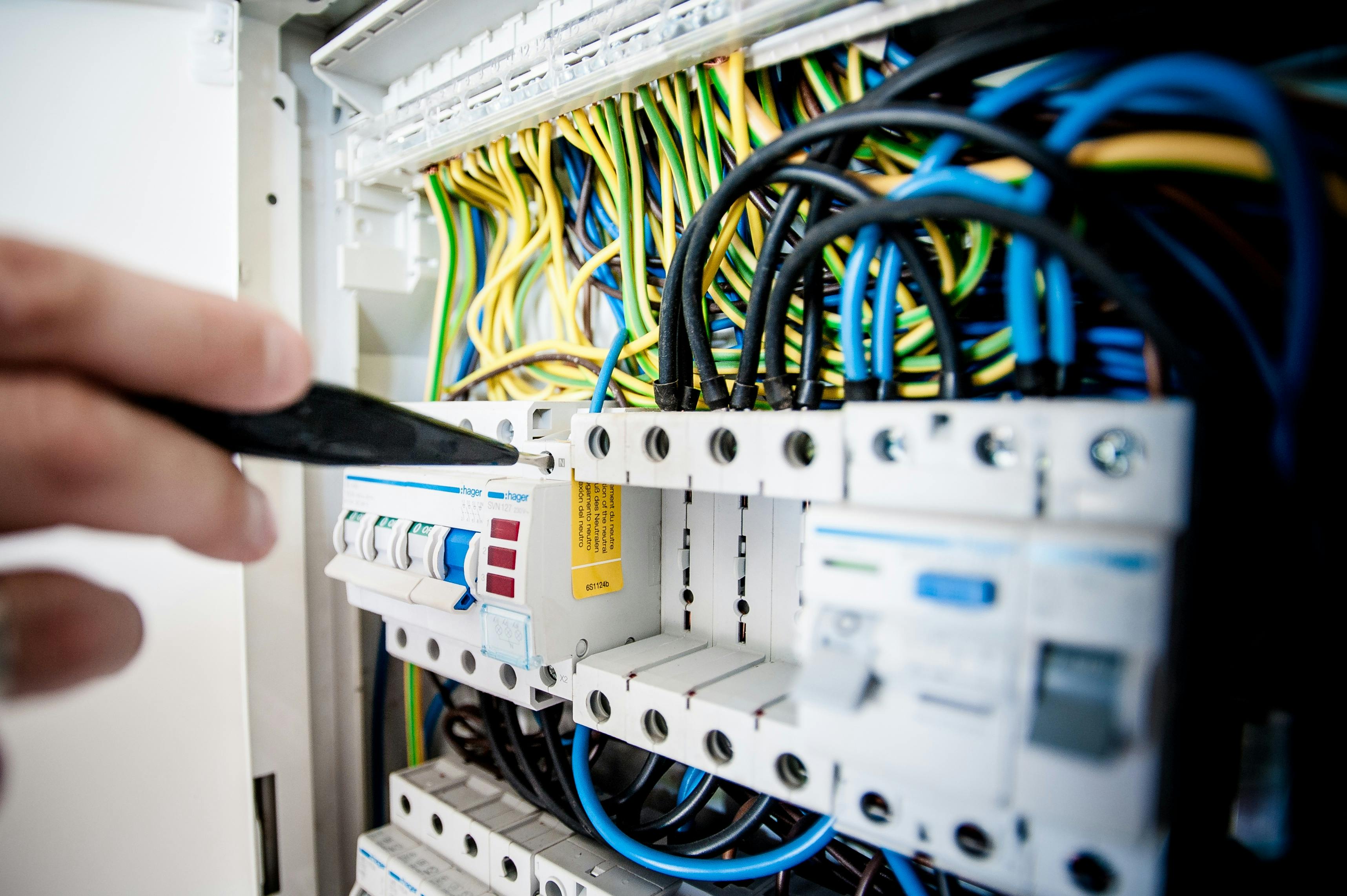 Professionell elinstallationer - Hand of electrician working on a circuit breaker panel with colorful wires, ensuring safe electrical connections.