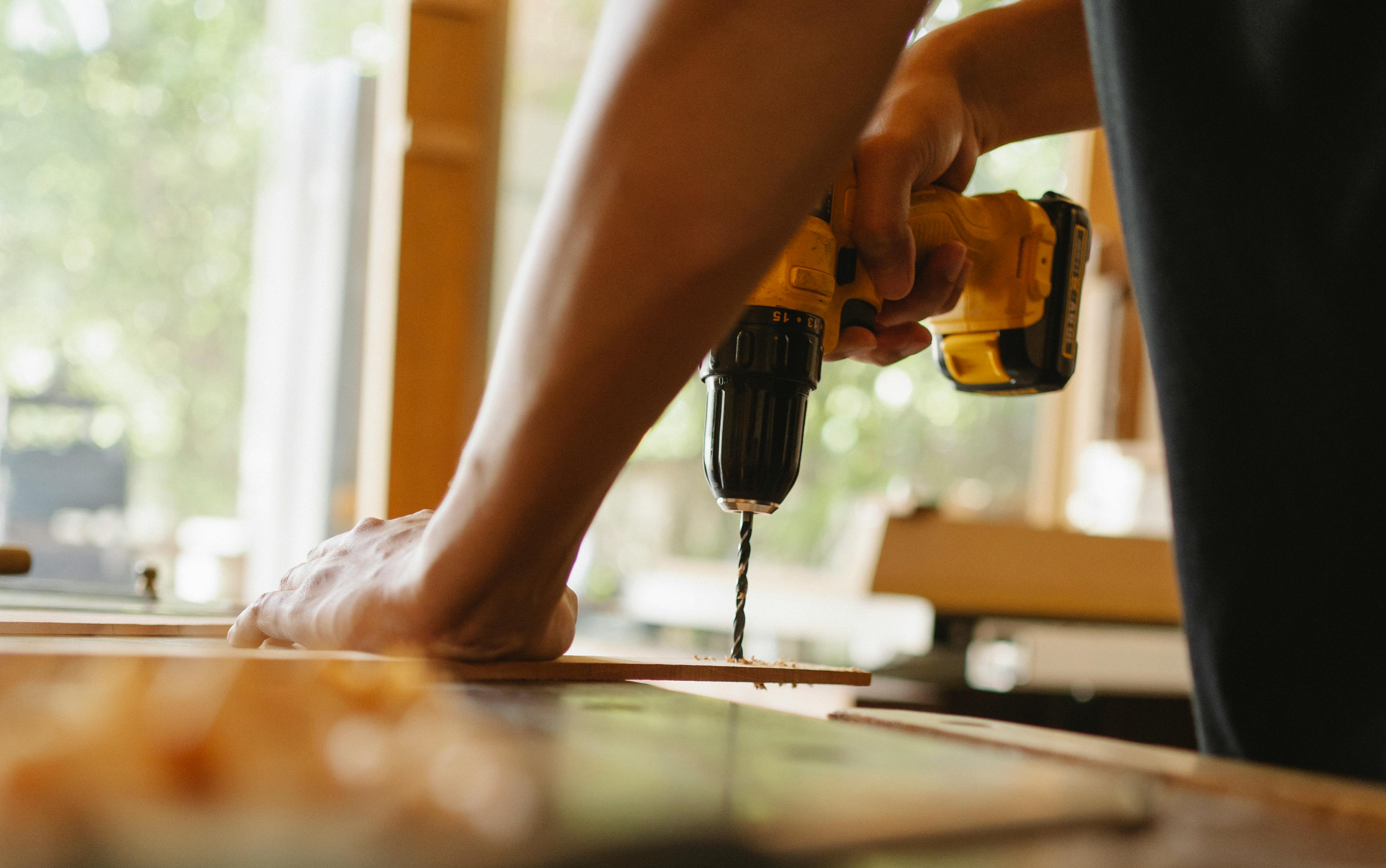 Professionell golvläggning - Close-up of a person using a power drill on wood indoors during daytime.