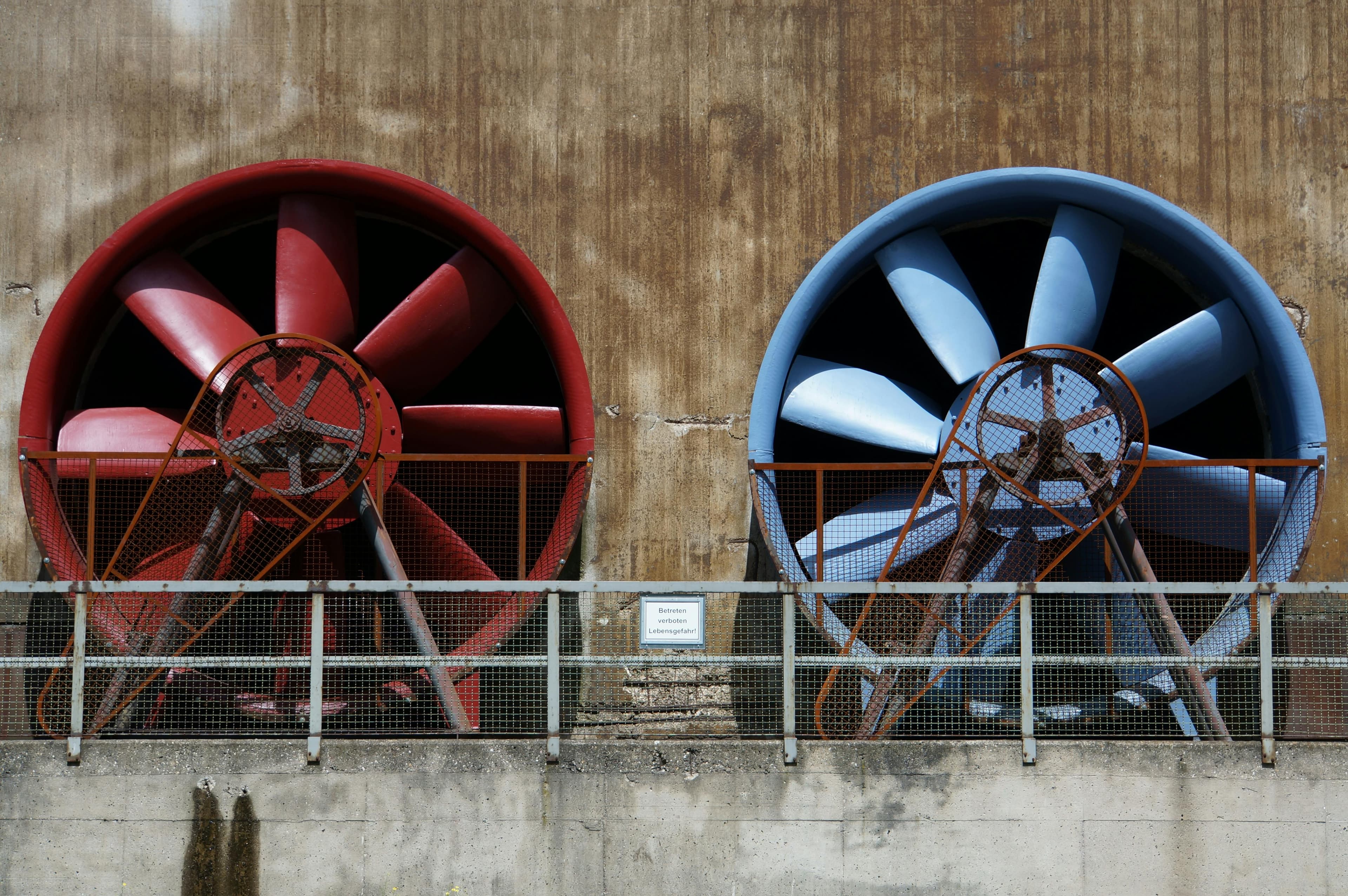 Professionell ventilationsinstallation - Close-up of large red and blue industrial fans on a rustic wall showcasing machinery and ventilation.